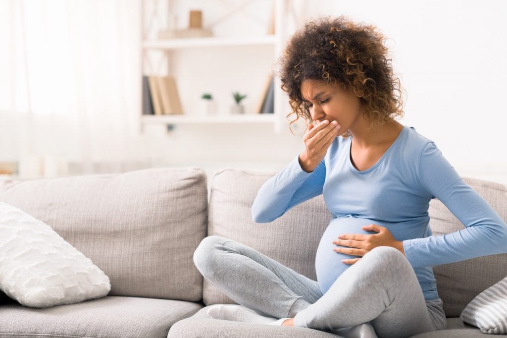 Young pregnant lady suffering with nausea, sitting on sofa, copy space
