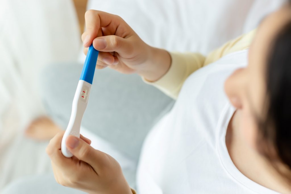 Happy pregnant woman holding pregnancy test, examine positive test, young lady has baby or fetus in belly. Young Mother waiting newborn baby prenatal, pregnancy, motherhood, expecting concept
