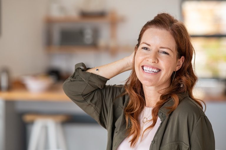 A smiling middle-aged woman in a bright home setting, representing health and wellness during perimenopause and menopause.