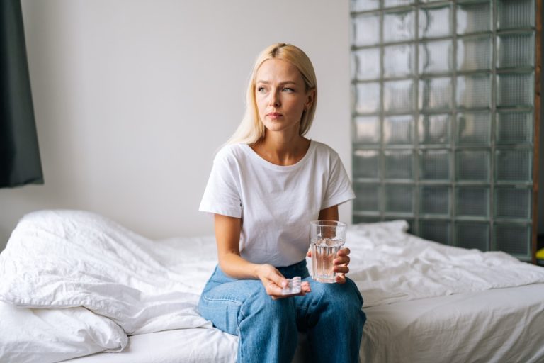 A woman taking emergency contraception pills with a glass of water in her bedroom.