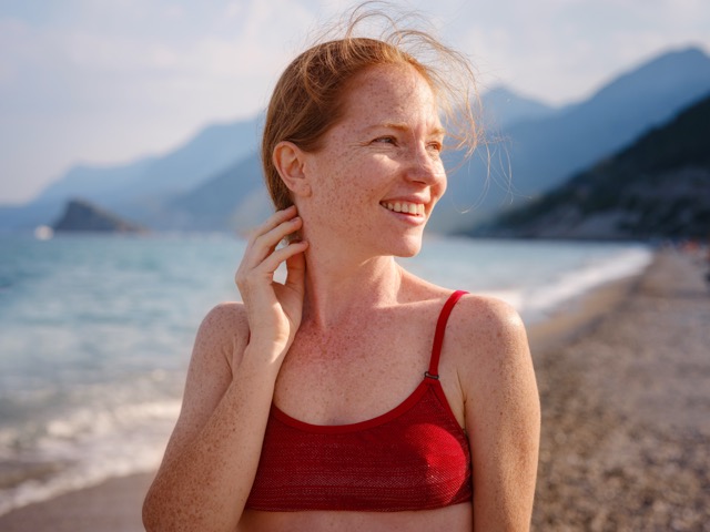 Smiling young woman enjoying the sun, representing body positivity and personal wellness.