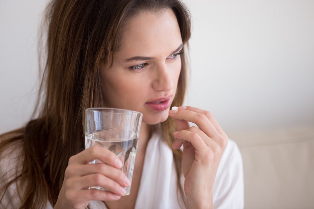 Woman considering emergency contraception, holding a pill and glass of water.