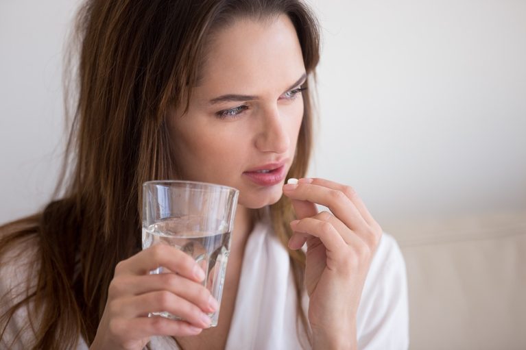 Woman considering emergency contraception, holding a pill and glass of water.