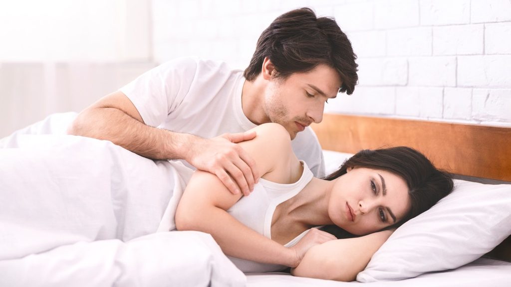 Woman experiencing low libido and emotional distance while lying in bed with her partner.